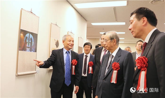 “湖州印象”攝影展主創(chuàng)、世界華人攝影協(xié)會副會長馮學(xué)敏向吳江浩大使、福田康夫前首相等嘉賓介紹展出作品。（人民網(wǎng) 許可攝）
