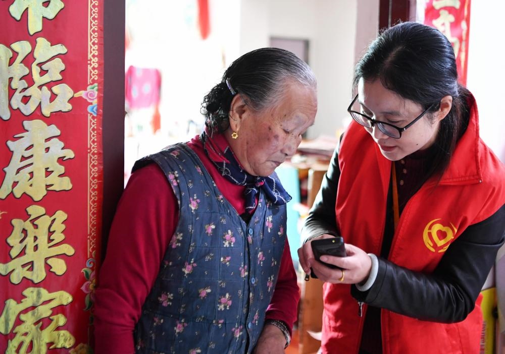 在福州市長(zhǎng)樂(lè)區(qū)航城街道籌岐村，智慧養(yǎng)老平臺(tái)派駐社區(qū)的助老員（右）在為老人陳鳳英（左）講解養(yǎng)老定制手機(jī)的用法（2021年11月26日攝）。新華社記者 魏培全 攝