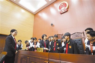圖③：同學(xué)們穿法袍、敲法槌，爭(zhēng)做“小法官”。