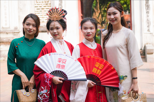 身穿古裝的中國(guó)游客和身穿越南傳統(tǒng)服飾奧黛的越南青年在文廟門前合影。