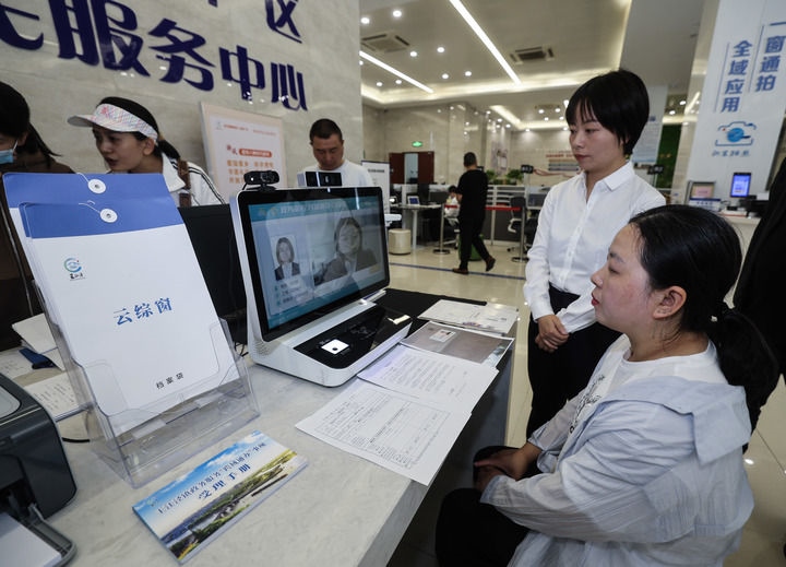 在浙江省嘉興市秀洲區(qū)王江涇鎮(zhèn)便民服務(wù)中心的“跨域通辦·云綜窗”窗口，辦理開業(yè)登記的個體工商戶（右一）通過該系統(tǒng)與江蘇省蘇州市吳江區(qū)盛澤鎮(zhèn)行政審批局工作人員視頻連線，進行身份讀取及材料線上審核（2024年5月9日攝）。新華社記者 徐昱 攝