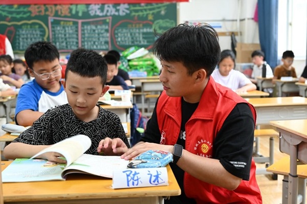 鄭州市二七區(qū)暑托班的志愿者輔導(dǎo)孩子寫作業(yè)。人民網(wǎng)記者王玉興攝